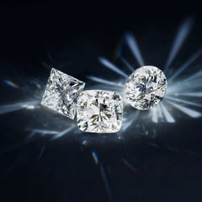 Three sparkling cut diamonds against a dark background with radiant light reflections.